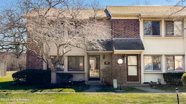 view of front of property featuring brick siding, roof with shingles, a front yard, and entry steps