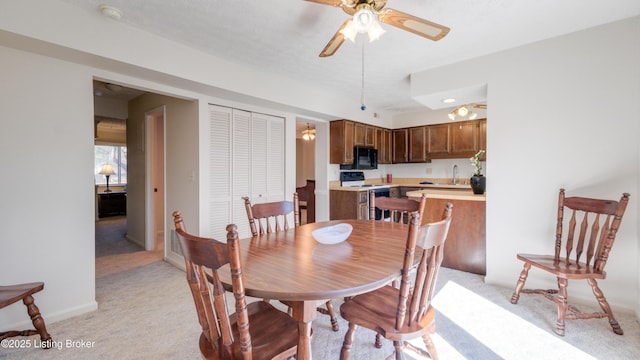 dining space featuring light colored carpet, baseboards, and ceiling fan