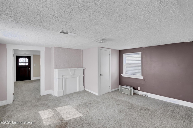 carpeted empty room with a wall mounted air conditioner, visible vents, baseboards, and a textured ceiling