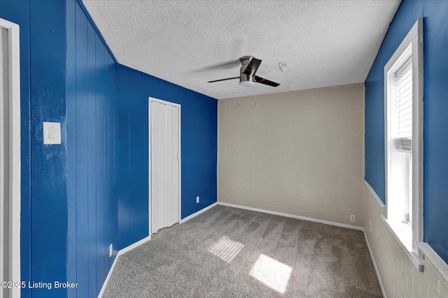 carpeted empty room with a ceiling fan, a textured ceiling, and brick wall