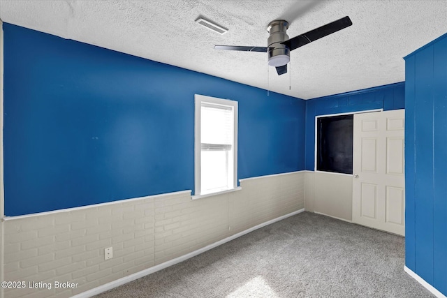 unfurnished bedroom featuring a ceiling fan, a wainscoted wall, carpet flooring, and visible vents