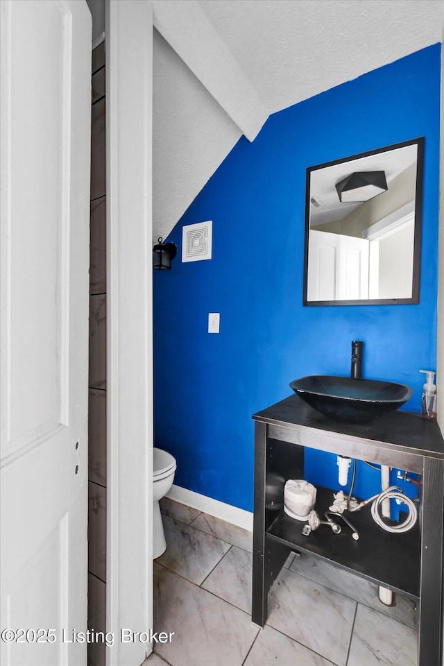 bathroom with vaulted ceiling, vanity, toilet, and baseboards