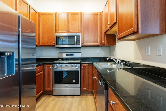 kitchen featuring appliances with stainless steel finishes, light wood-type flooring, brown cabinetry, and a sink