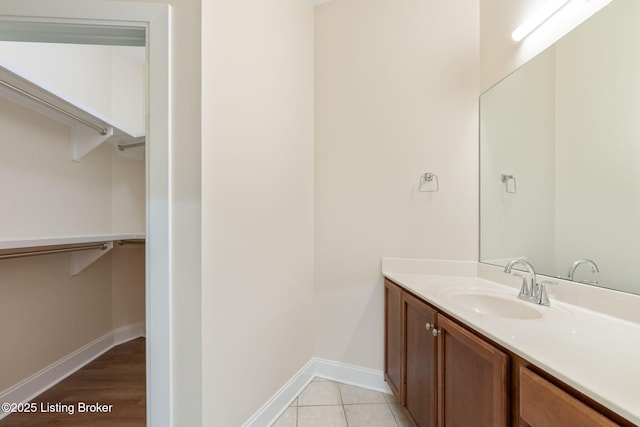 bathroom with tile patterned flooring, a spacious closet, baseboards, and vanity