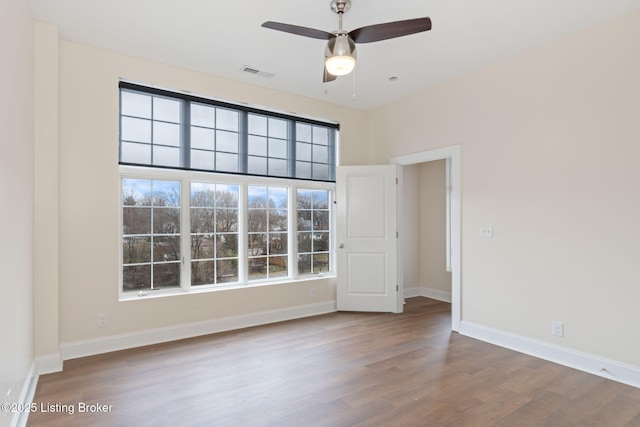 spare room featuring baseboards, visible vents, ceiling fan, and wood finished floors