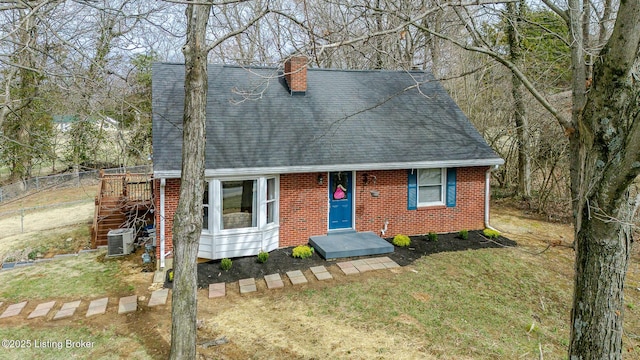 cape cod home featuring a shingled roof, a chimney, central air condition unit, a front lawn, and brick siding