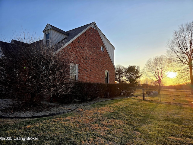 view of side of home with a gate, fence, a lawn, and brick siding