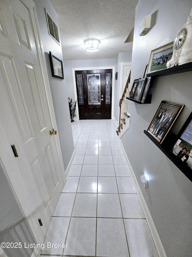 corridor featuring light tile patterned floors, a textured ceiling, visible vents, baseboards, and stairs