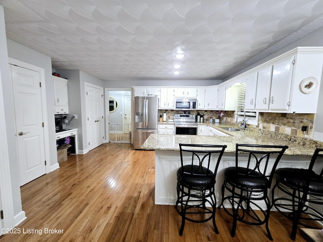 kitchen featuring light wood-style flooring, decorative backsplash, appliances with stainless steel finishes, a sink, and a peninsula