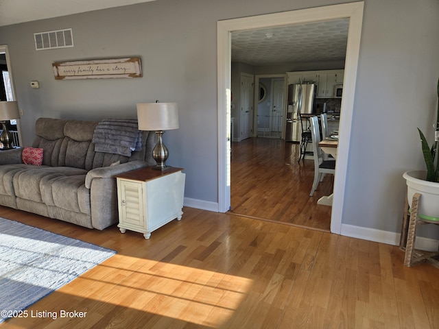 living room with visible vents, baseboards, and wood finished floors