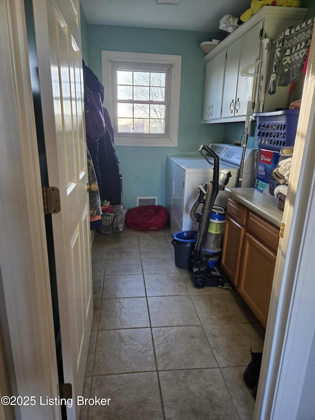 clothes washing area featuring visible vents, light tile patterned flooring, washing machine and clothes dryer, and cabinet space