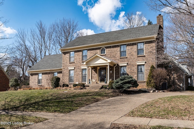 view of front of house with cooling unit, brick siding, a shingled roof, a chimney, and a front yard