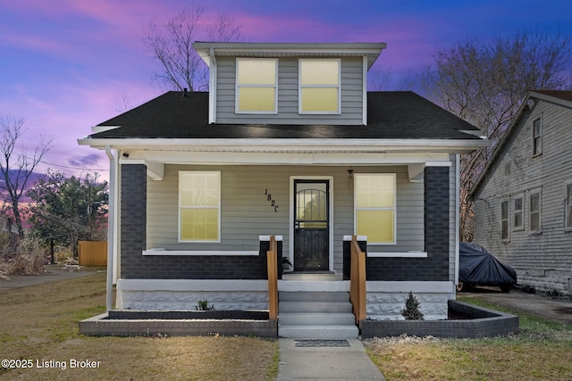 bungalow-style house with brick siding, covered porch, and a shingled roof