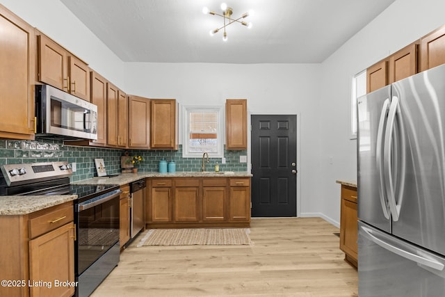 kitchen featuring light wood finished floors, backsplash, appliances with stainless steel finishes, brown cabinetry, and a sink