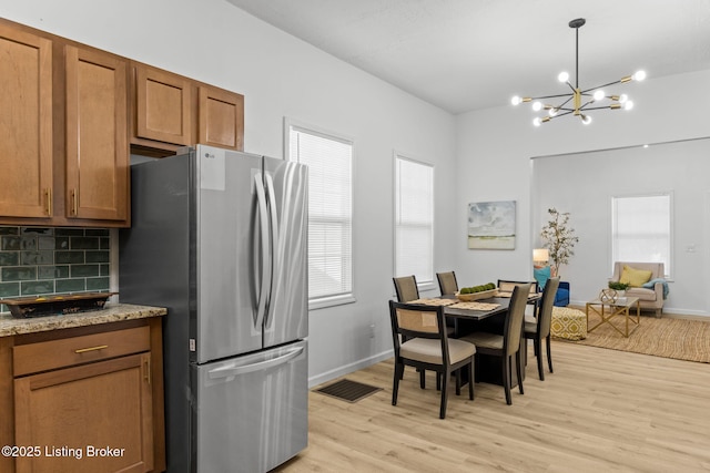 kitchen with visible vents, brown cabinets, light wood-type flooring, freestanding refrigerator, and tasteful backsplash