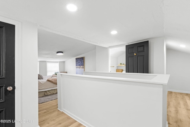 hallway with vaulted ceiling, light wood-style flooring, recessed lighting, and an upstairs landing