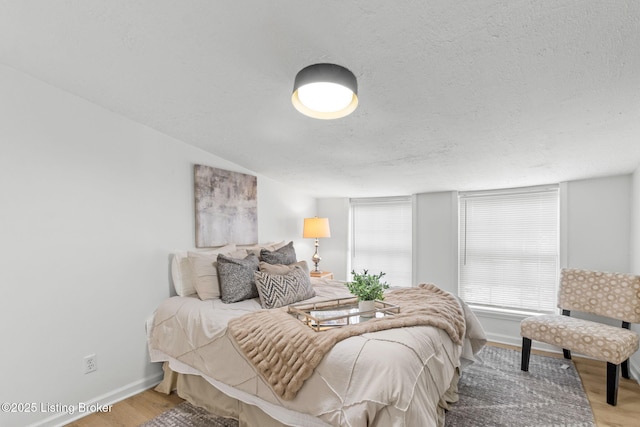 bedroom with wood finished floors, baseboards, and a textured ceiling