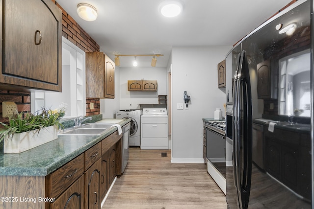 kitchen with range with gas stovetop, dark countertops, light wood-type flooring, separate washer and dryer, and a sink