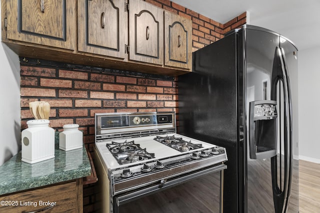 kitchen featuring white gas stove, baseboards, light wood-style floors, black refrigerator with ice dispenser, and dark countertops