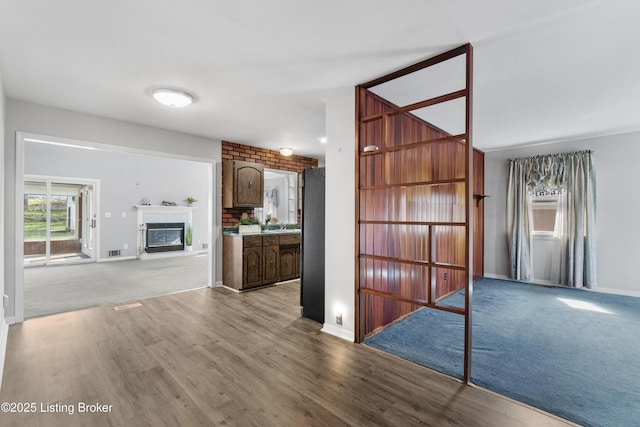 unfurnished living room featuring a glass covered fireplace, visible vents, baseboards, and wood finished floors