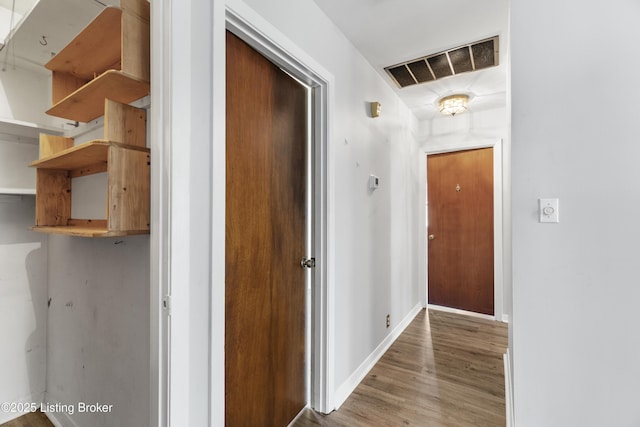 hall featuring visible vents, baseboards, and wood finished floors