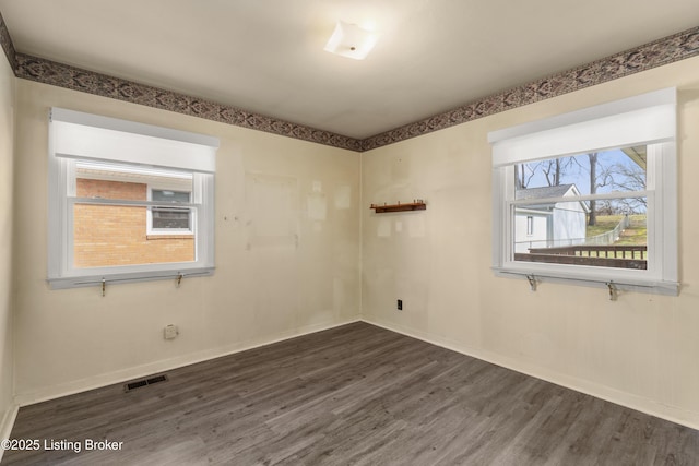 empty room featuring dark wood-style floors, visible vents, and baseboards