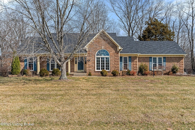 view of front facade featuring a shingled roof, a front yard, and brick siding