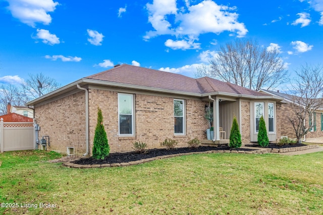 ranch-style home featuring a front lawn, roof with shingles, fence, and brick siding