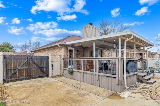 exterior space with brick siding, a chimney, a gate, fence, and a wooden deck