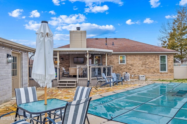 back of house featuring brick siding, fence, a wooden deck, and a covered pool