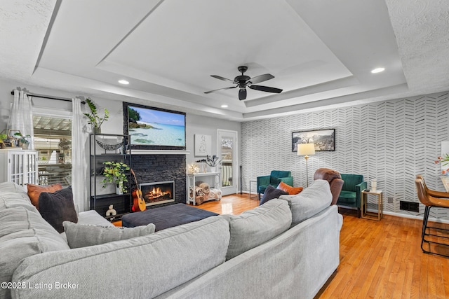 living room featuring a tray ceiling, a glass covered fireplace, and light wood finished floors