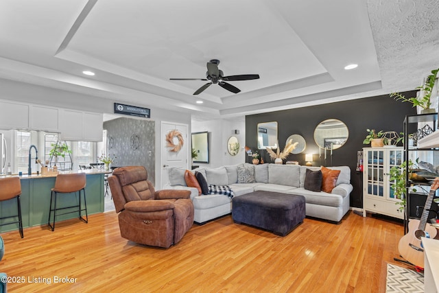 living area featuring light wood-style floors, a tray ceiling, ceiling fan, and recessed lighting