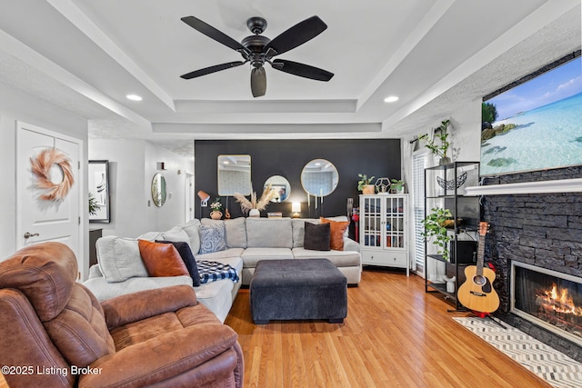 living area with light wood-style floors, a tray ceiling, ceiling fan, and a stone fireplace