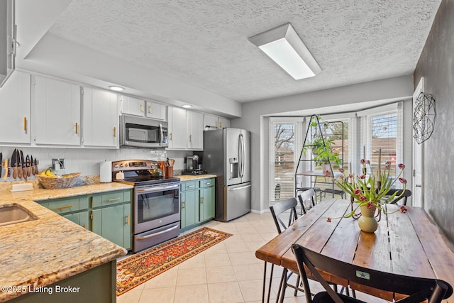 kitchen with light tile patterned floors, appliances with stainless steel finishes, light countertops, white cabinetry, and backsplash