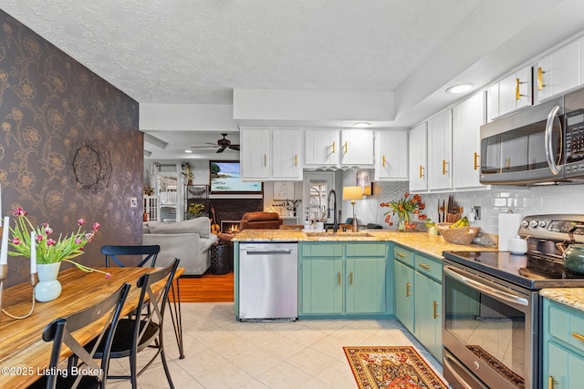 kitchen featuring wallpapered walls, white cabinets, stainless steel appliances, a textured ceiling, and a sink