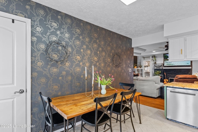 dining room with a fireplace, a ceiling fan, light tile patterned flooring, a textured ceiling, and wallpapered walls