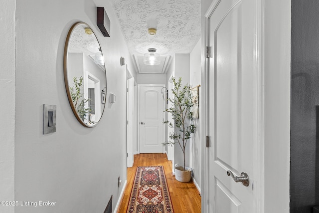 hall with light wood-style floors, baseboards, and a textured ceiling