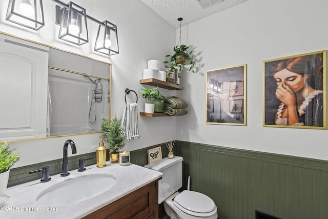 full bath featuring toilet, a wainscoted wall, curtained shower, a textured ceiling, and vanity