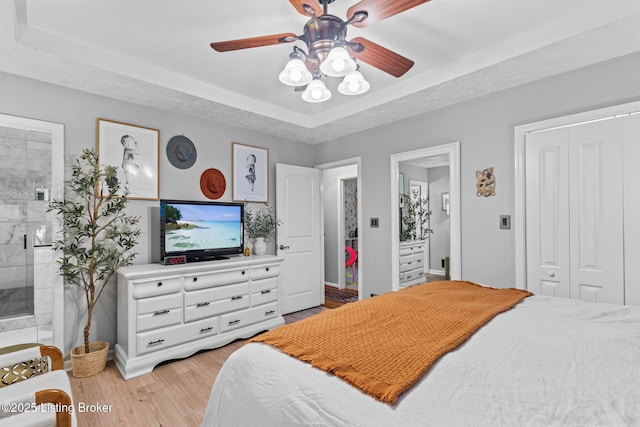 bedroom with a textured ceiling, ensuite bathroom, a closet, light wood-type flooring, and a raised ceiling