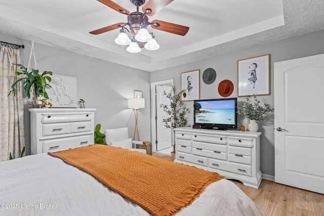 bedroom featuring ceiling fan, a textured ceiling, baseboards, a tray ceiling, and light wood finished floors