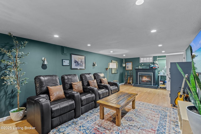 living area with a warm lit fireplace, baseboards, wood finished floors, and recessed lighting