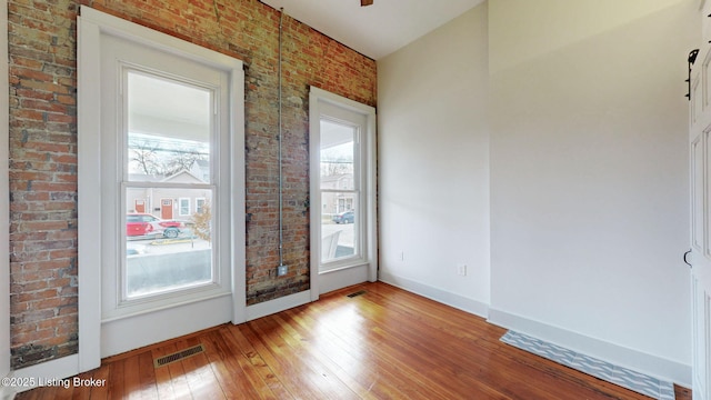 spare room featuring baseboards, brick wall, visible vents, and hardwood / wood-style floors