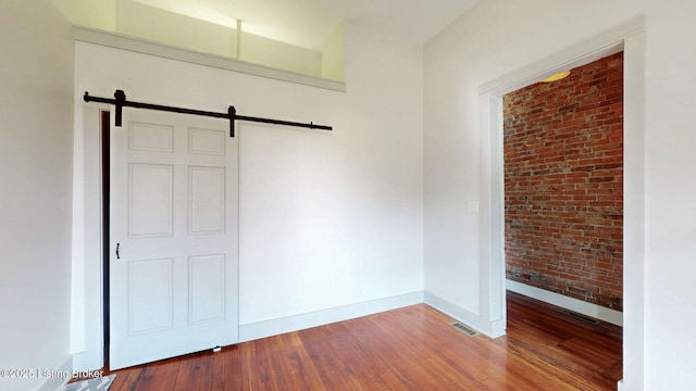 unfurnished bedroom featuring a barn door, visible vents, brick wall, and hardwood / wood-style flooring