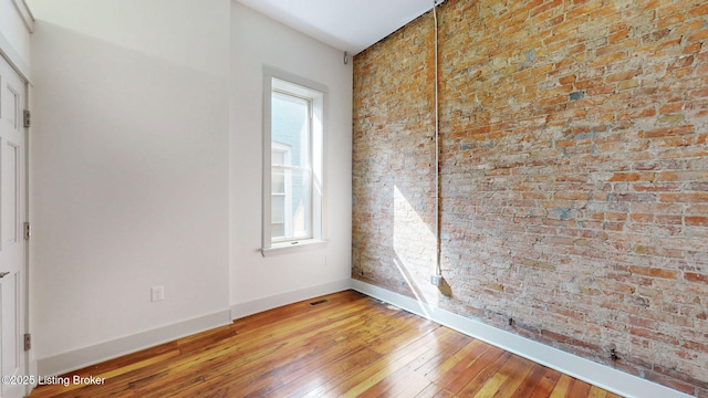 unfurnished room with visible vents, brick wall, light wood-style flooring, and baseboards