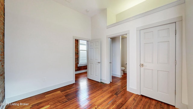 unfurnished bedroom with a high ceiling, hardwood / wood-style flooring, and baseboards