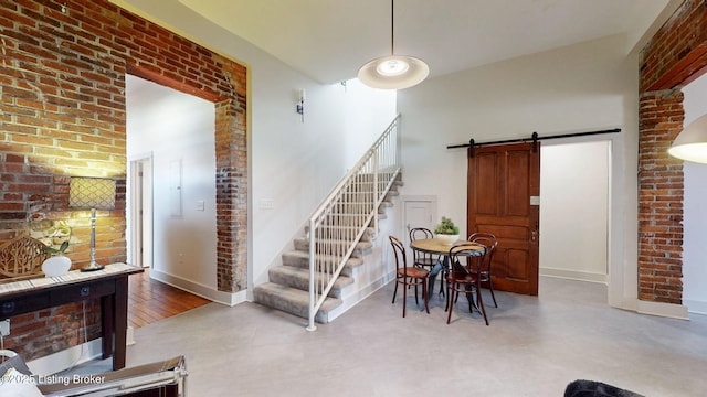 stairs featuring brick wall, a barn door, a high ceiling, and baseboards