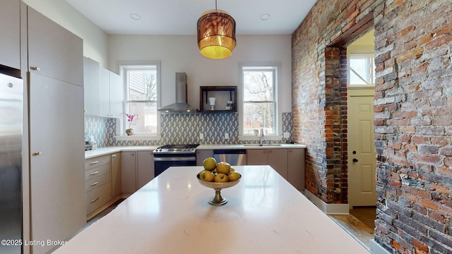 kitchen with stainless steel appliances, gray cabinets, light countertops, a sink, and wall chimney range hood