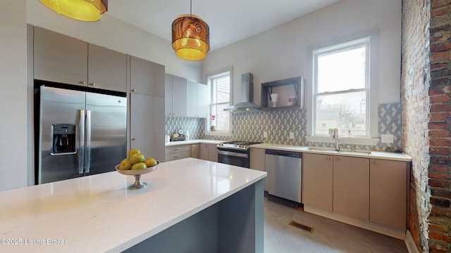 kitchen with gray cabinetry, a sink, appliances with stainless steel finishes, backsplash, and wall chimney exhaust hood