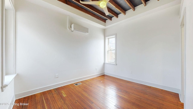 spare room featuring hardwood / wood-style floors, visible vents, beam ceiling, and an AC wall unit