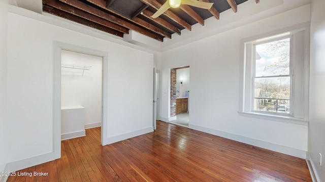 unfurnished bedroom with baseboards, hardwood / wood-style flooring, a spacious closet, beam ceiling, and a closet